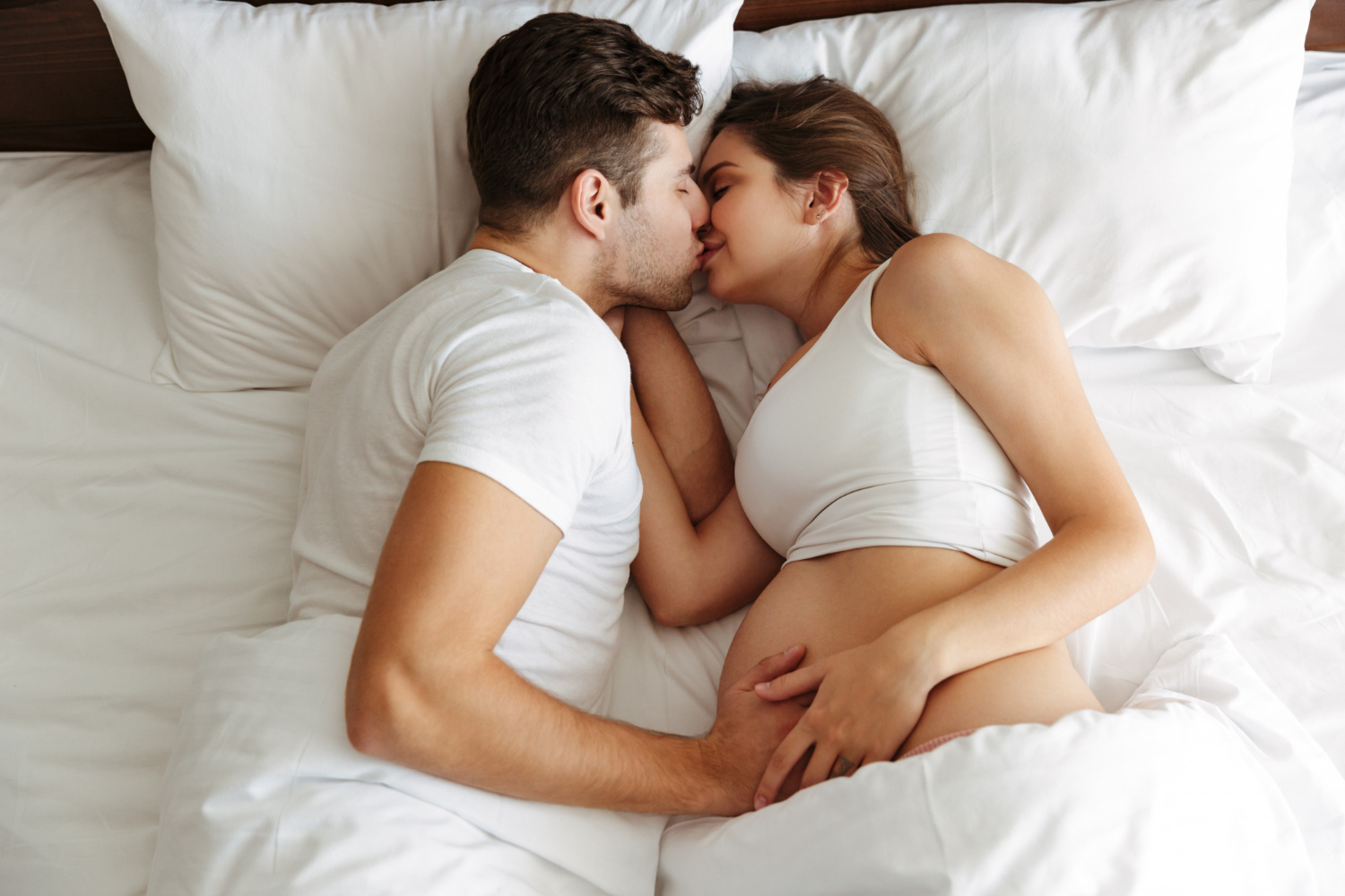парень целует беременную девушку в постели