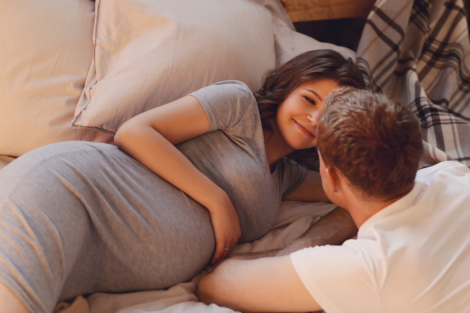беременная пара лежит на кровати и смотрит друг на друга